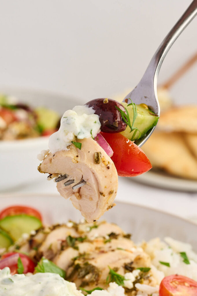 Greek chicken meal prep bowls with rice, vegetables, feta, and tzatziki.