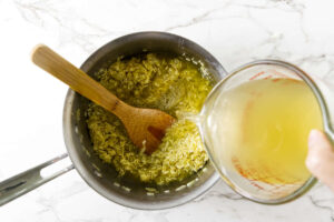 Chicken broth being poured into toasted rice for Greek lemon rice.