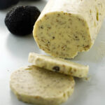 Truffle butter log with herbs, two slices, and whole black truffles nearby.