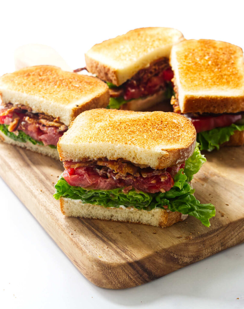 Homemade BLT sandwich sliced in half with bacon, lettuce, and ripe tomato.