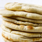 Close-up stack of soft homemade pita bread with lightly browned spots.