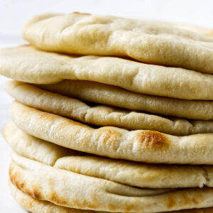 Close-up stack of soft homemade pita bread with lightly browned spots.
