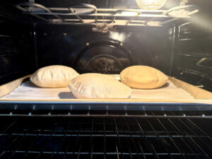 Pita bread puffing in a hot oven on a sheet pan.