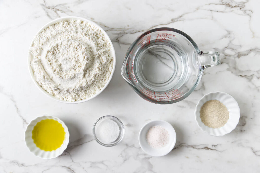 Ingredients for homemade pita bread with flour, water, olive oil, yeast, sugar, and salt.
