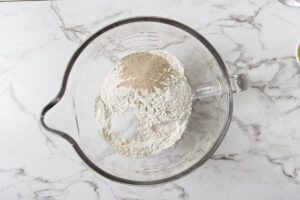 Bread flour, yeast, sugar, and salt in a stand mixer bowl for pita dough.