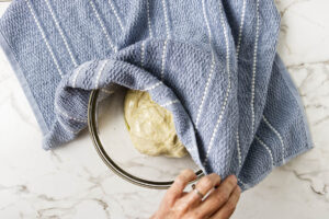 Risen pita dough in a bowl being uncovered after the first rise.