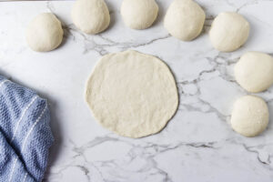 Pita dough balls and one rolled round ready for shaping.