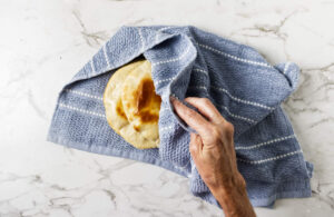 Hand lifting soft pita bread from a towel-lined stack.
