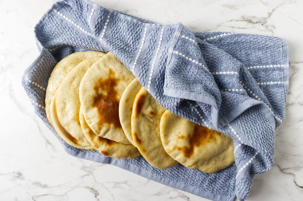 Warm pita bread stacked under a towel to keep it soft.