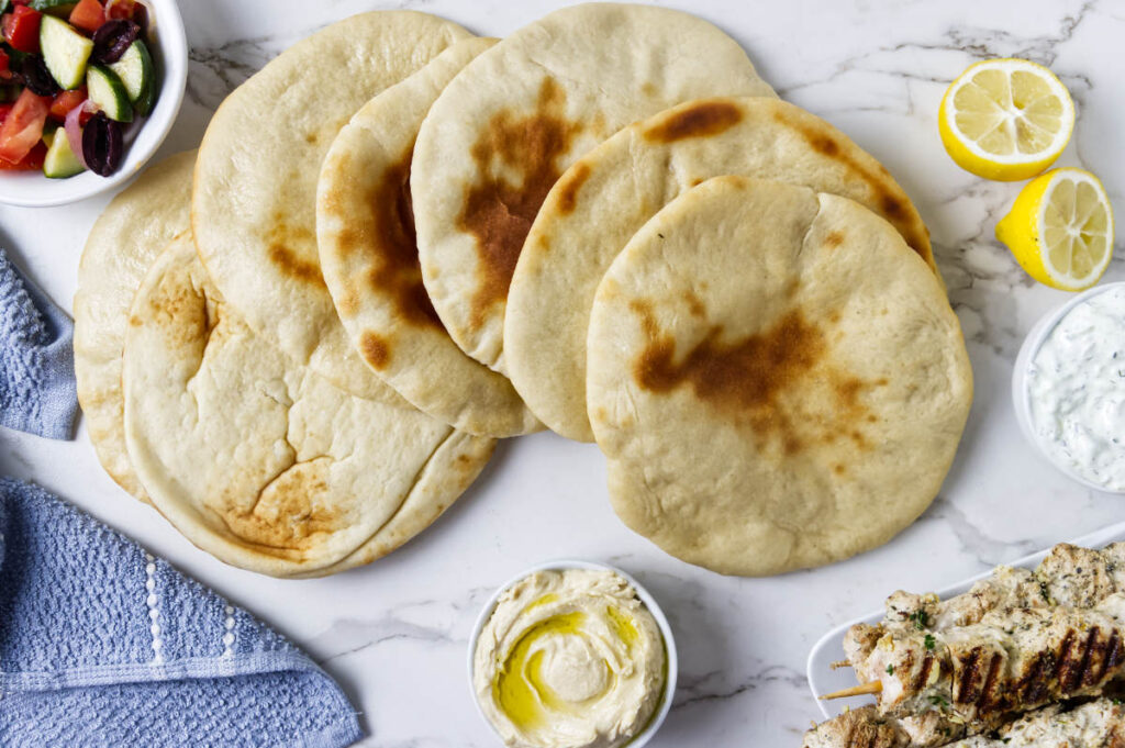 Homemade pita bread served with olive oil, herbs, and lemon wedges.