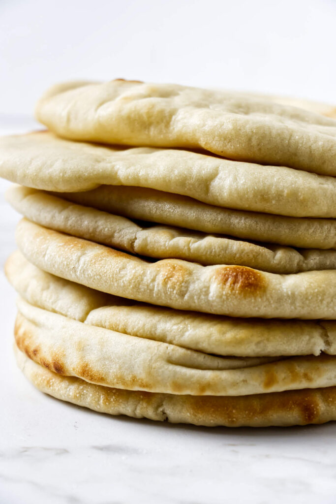 Soft pita bread stacked on a white surface with golden brown spots.