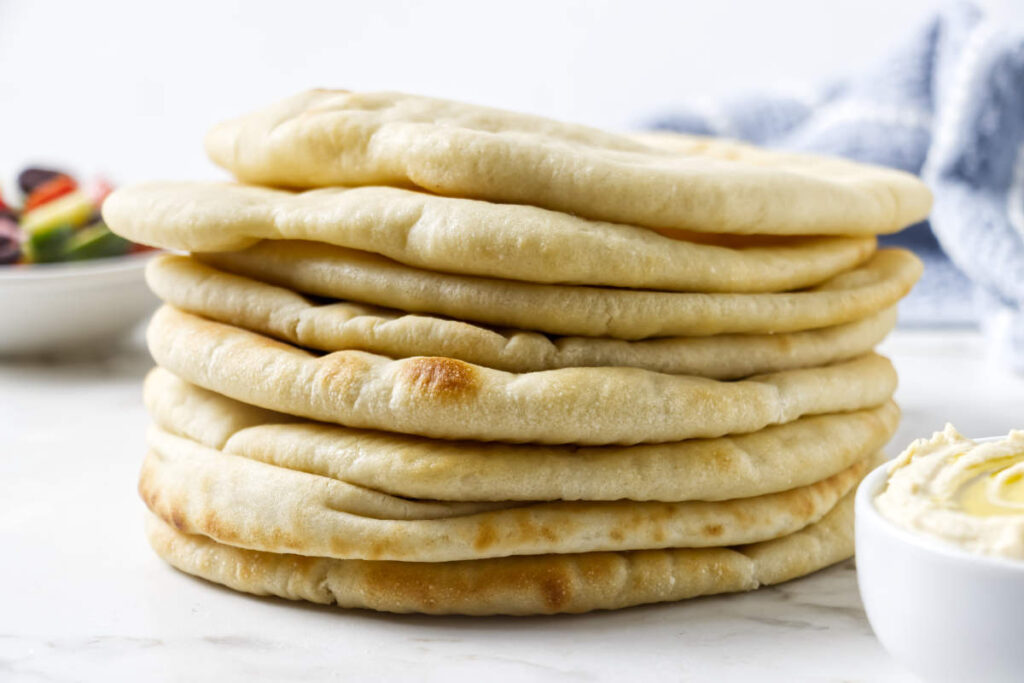 Stack of homemade pita bread served with a bowl of dip.