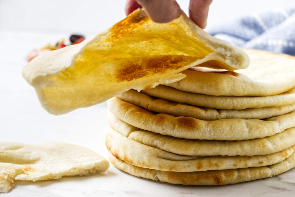Fresh pita bread pocket held above a stack of warm pitas.