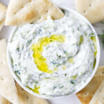 Bowl of tzatziki sauce with olive oil, pita bread on the side.