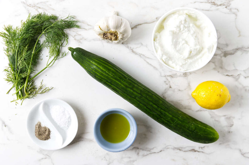 Cucumber, lemon, garlic, dill, yogurt, olive oil, salt and pepper displayed.