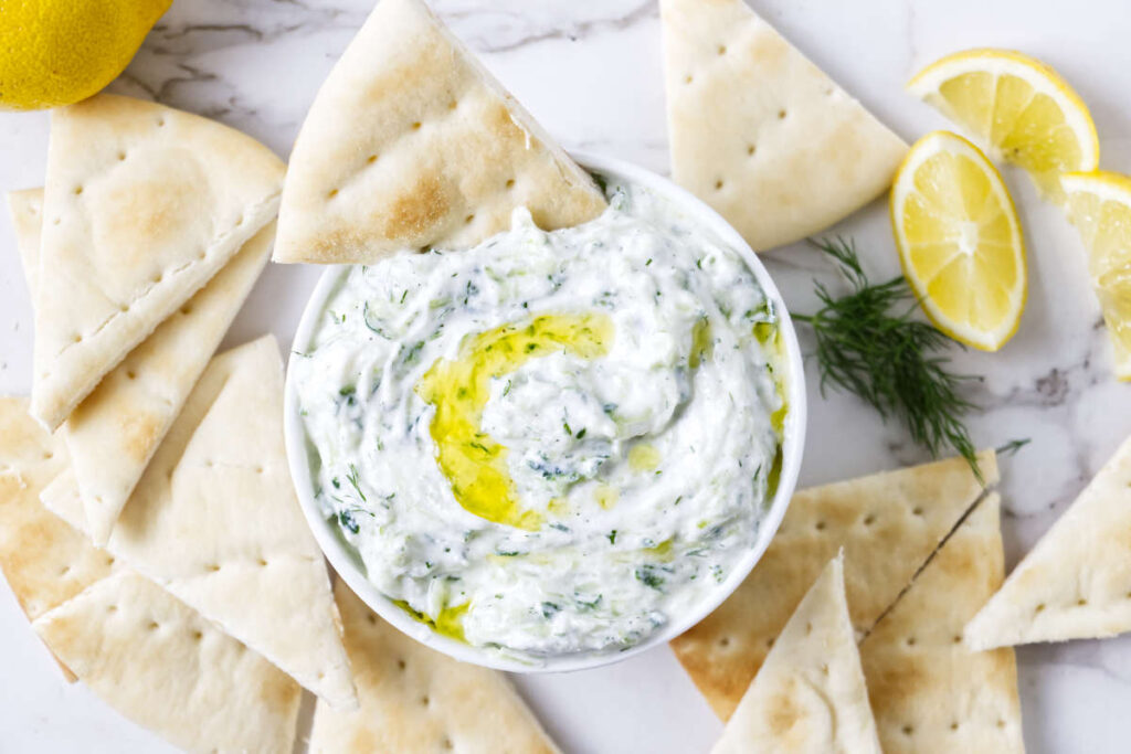 Tzatziki sauce in a bowl with olive oil, pita, lemon, and dill.