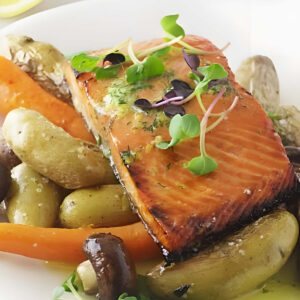 A salmon fillet on a pile of roasted veggies and topped with dill butter.
