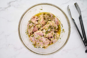 Chicken coated in lemon Greek marinade in a mixing bowl.