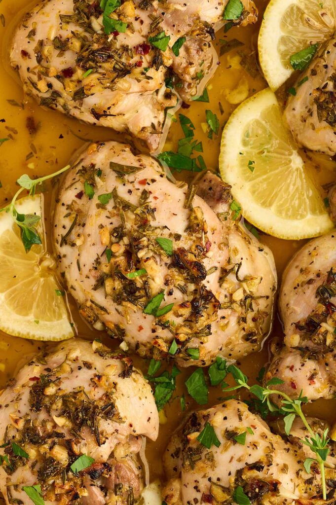 Boneless chicken thighs marinating with lemon, garlic, rosemary, thyme, and oregano.