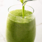 Green smoothie poured into clear glass.