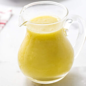 Glass pitcher of preserved lemon dressing on white surface, red-striped napkin behind.