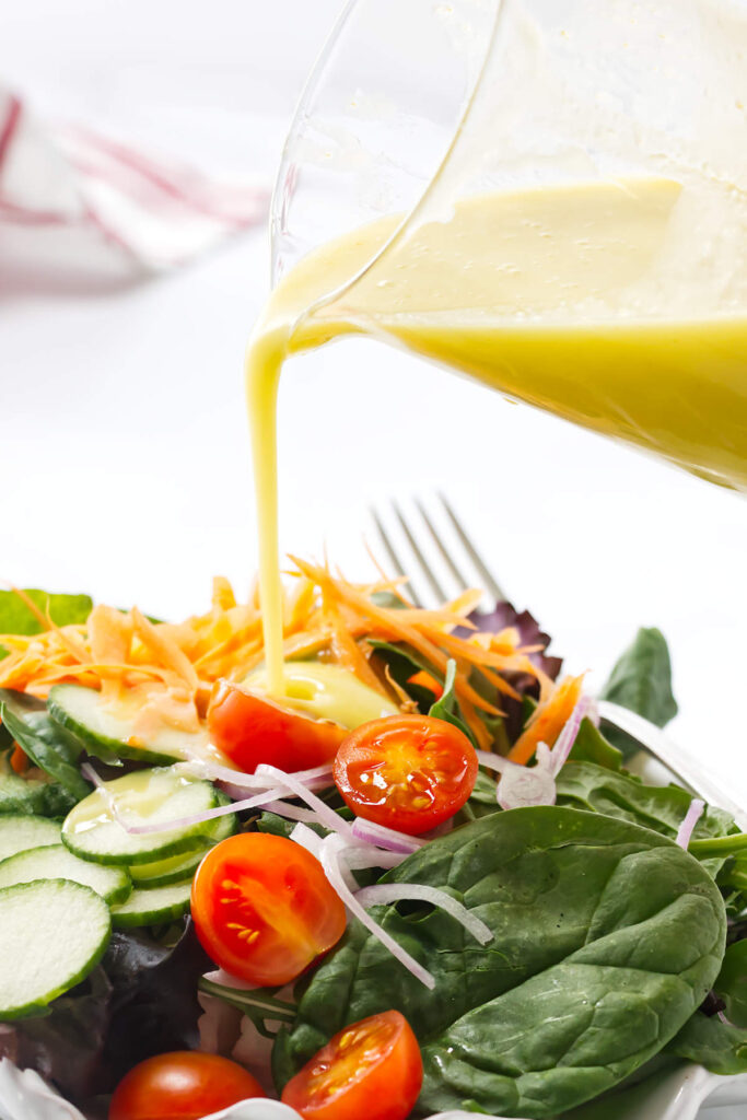 Pouring homemade lemon vinaigrette over a green salad.