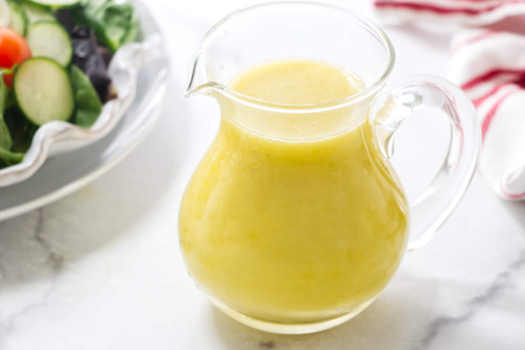 Glass pitcher of creamy salad dressing made with preserved lemons.