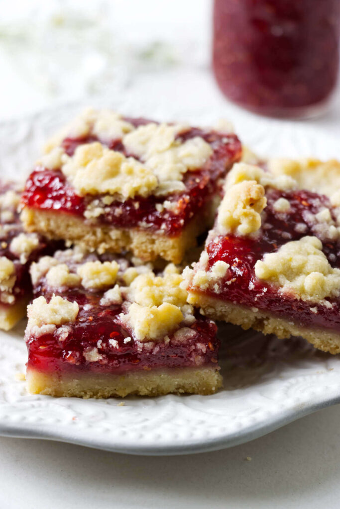 Raspberry crumble bars stacked on a plate with a jam filling and crumb topping.