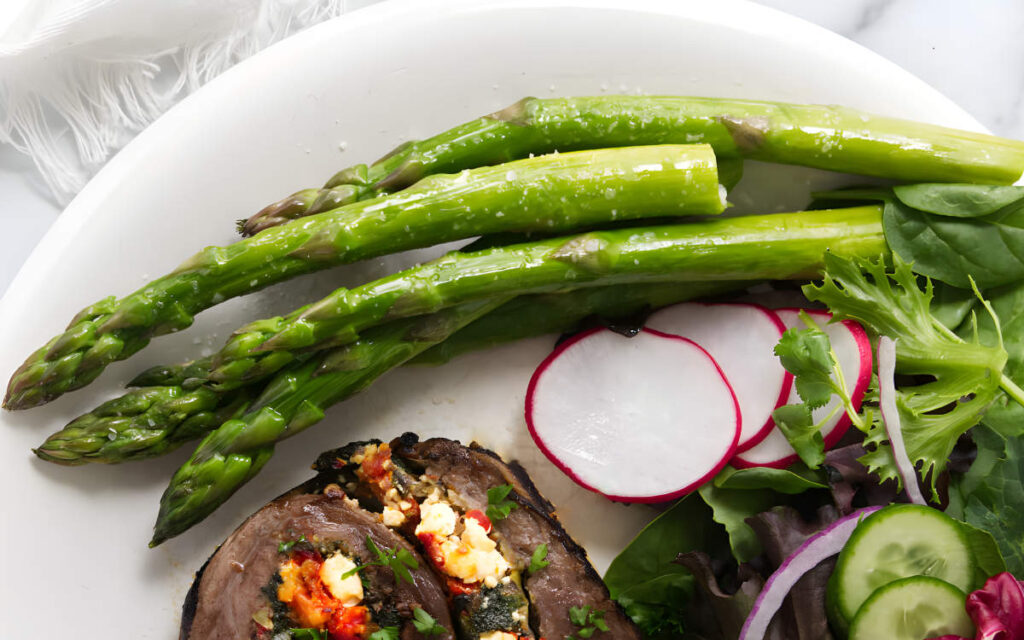 Plate with asparagus, radish slices, mixed greens, cucumber, and stuffed meat.