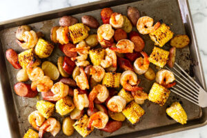 Shrimp, corn, sausage, and potatoes roasting on a sheet pan.