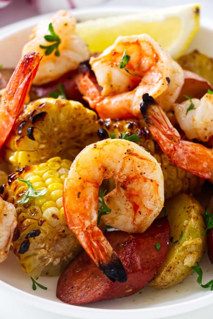 Shrimp boil sheet pan dinner served with lemon wedges and chopped parsley.