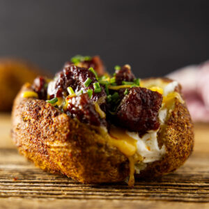 Baked potato with beef, cheese, sour cream, and chives on wood.