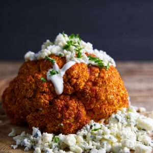 Whole smoked cauliflower with creamy dressing and herbs, blue cheese garnish.