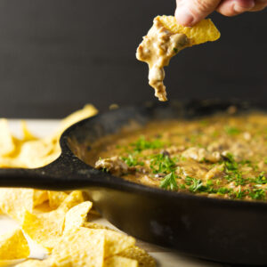 A hand dipping a chip into cheese dip.