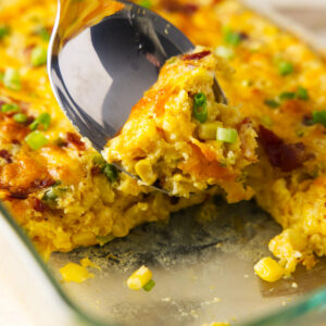 A spoon scooping corn casserole from a dish.