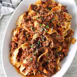 Wide noodles with ragu meat sauce, cheese, and herbs on oval platter.