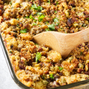 A wooden spoon scooping cornbread stuffing from a casserole dish.