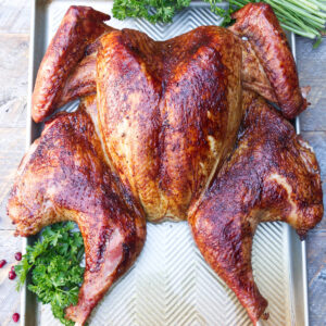 Spatchcocked turkey with crispy skin on tray, garnished with parsley and cranberries.