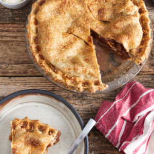 Apple pie with a slice on a plate, ice cream, and striped towel.