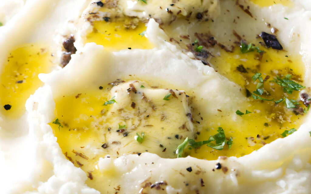 Mashed potatoes with melting truffle butter, herbs, and black pepper on top.