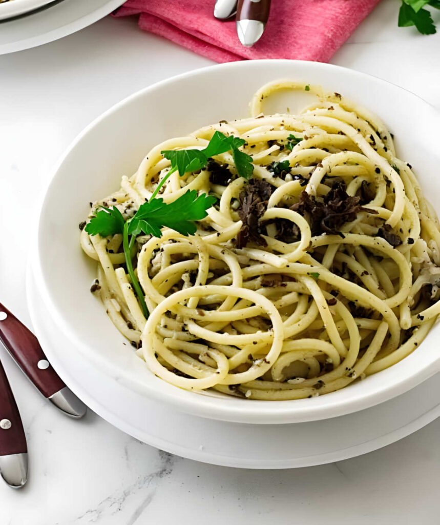 Spaghetti with black truffle butter and parsley in a white bowl.