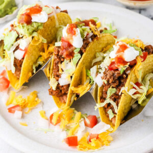 Crisp ground beef tacos with lettuce, cheese, tomatoes, sour cream, and salsa.