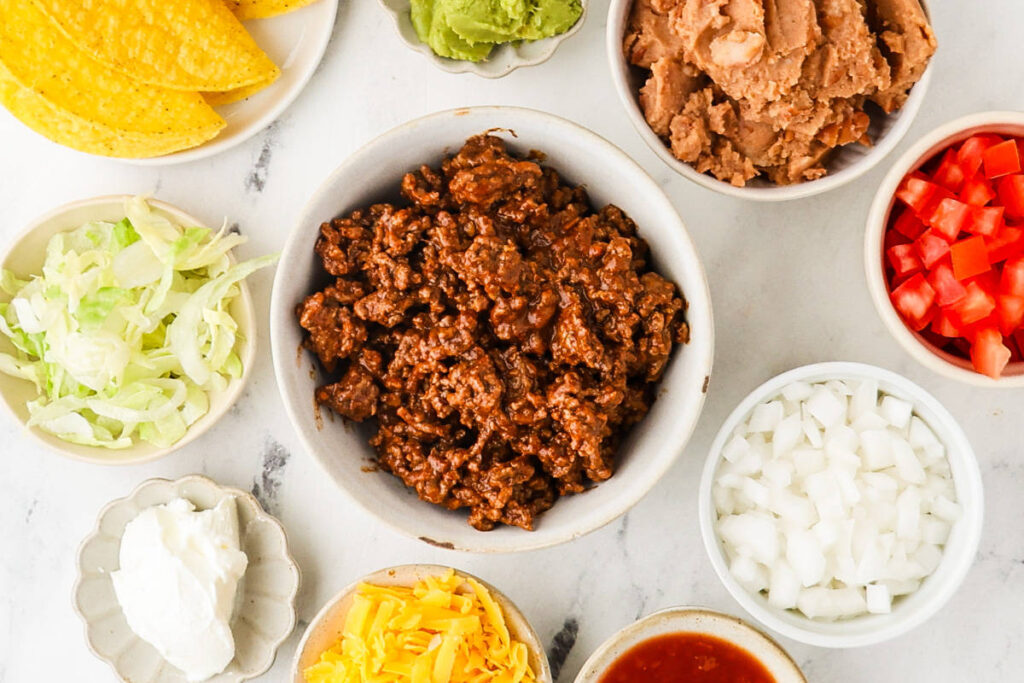 Taco night setup with seasoned ground beef, crisp shells, refried beans, and toppings.
