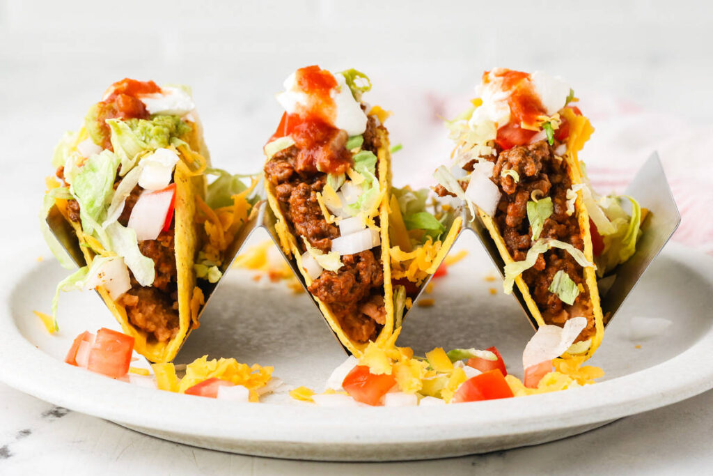 Three crispy ground beef tacos arranged on a serving platter.