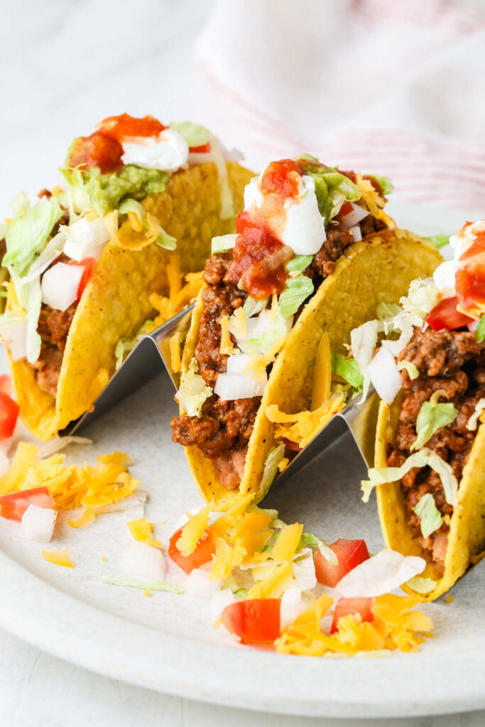 Ground beef tacos on a white plate with shredded lettuce, cheese, and salsa.