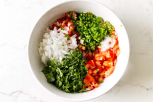 Adding chopped tomatoes, onions, cilantro, and jalapenos to a bowl for salsa fresca.