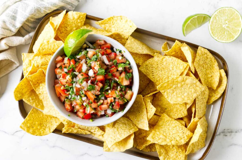 A bowl of Mexican pico de gallo surrounded by chips.