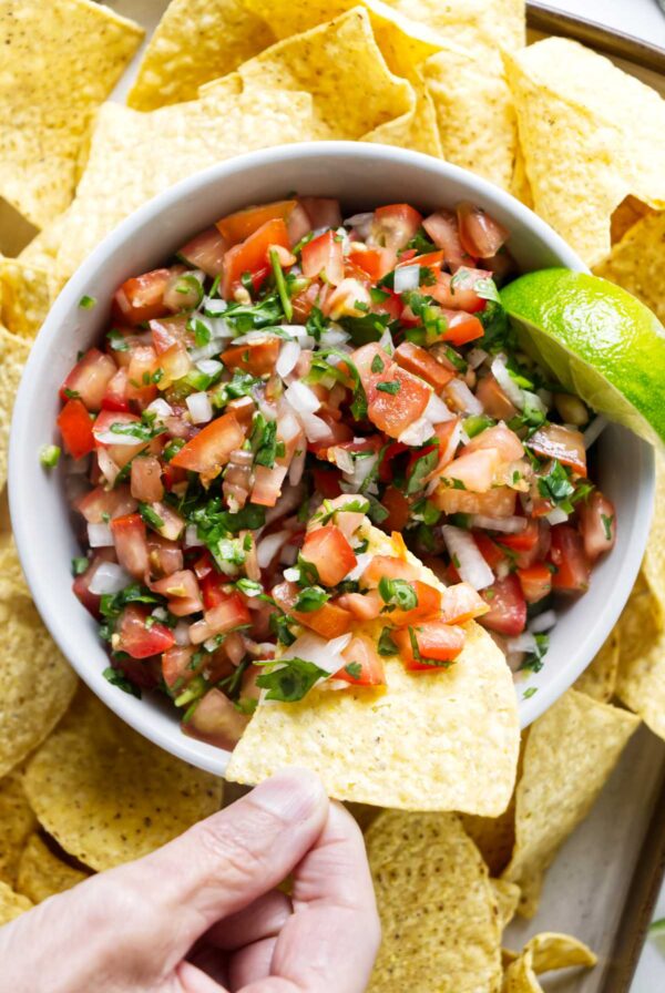A hand dipping a chip into fresh pico de gallo.