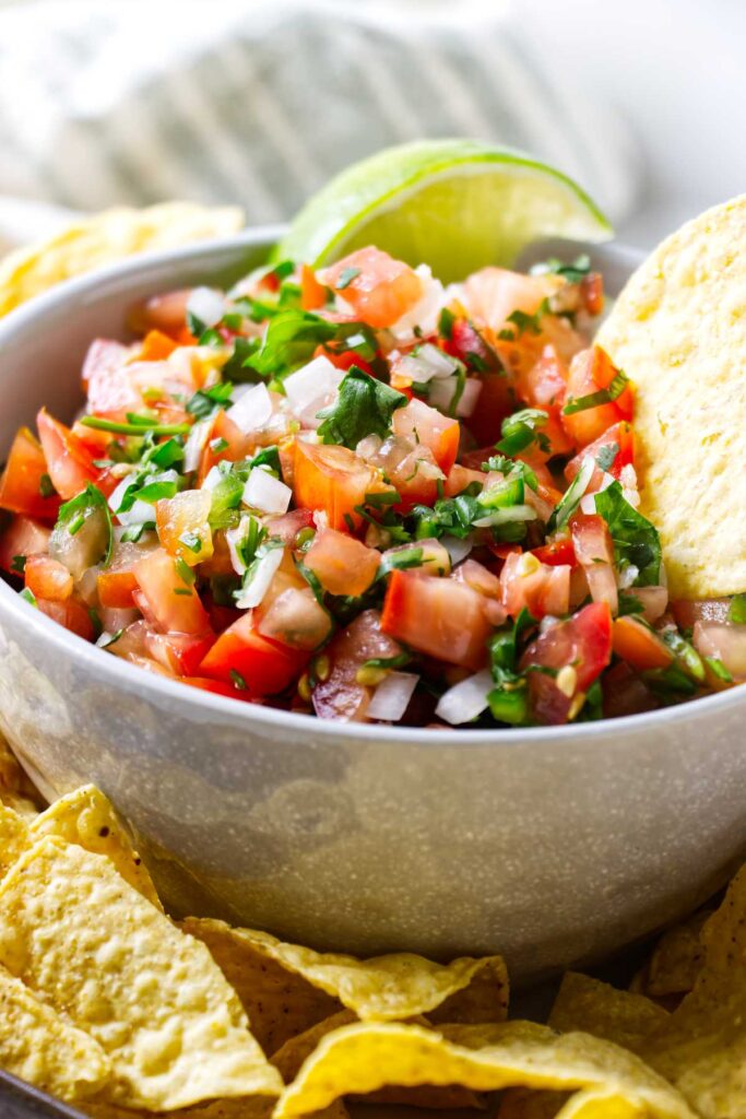 A serving bowl filled with spicy pico de gallo next to chips.