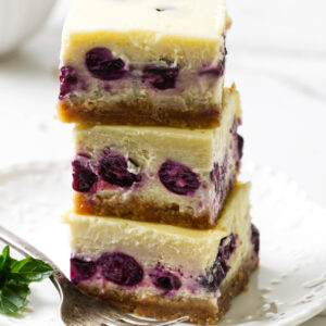Lemon blueberry cheesecake bars stacked on top of each other.